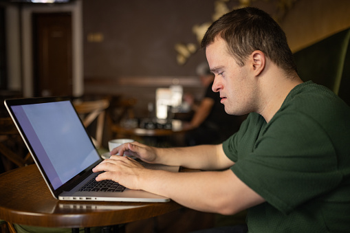 Charming man with down syndrome using laptop while sitting in cafe.