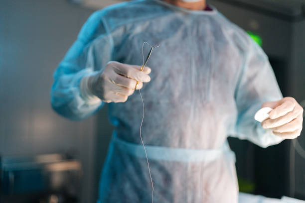 istock Closeup hands of unrecognizable professional surgeon wearing uniform holding forceps with suture thread on blurred background. 1933644208