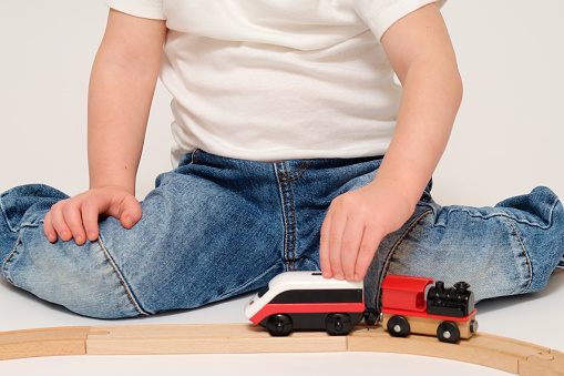 A child is playing train cars on the railway, studio white background. Baby with a toy train on a wooden railway