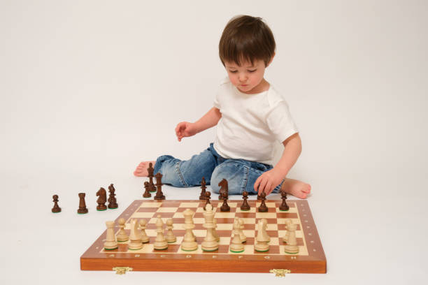 istock A child is playing chess, studio white background. Baby with chess pieces on a chessboard 1933648556