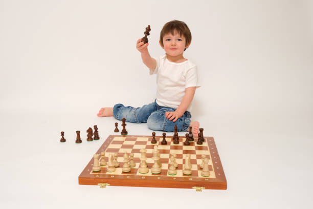 istock A child is playing chess, studio white background. Baby with chess pieces on a chessboard 1933648563