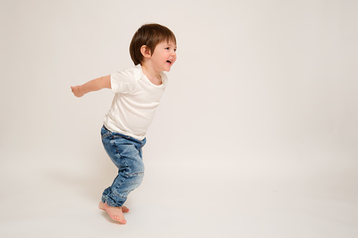 The child runs and jumps, studio white background. Happy baby running full-length with a smile on his face