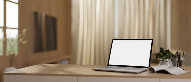 istock Modern home workspace with a white-screen laptop and stationery on a table in a modern living room. 1933727836
