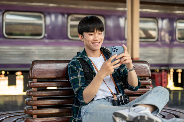 istock A happy Asian man is using his phone while waiting for his train at a railway station. 1933762188