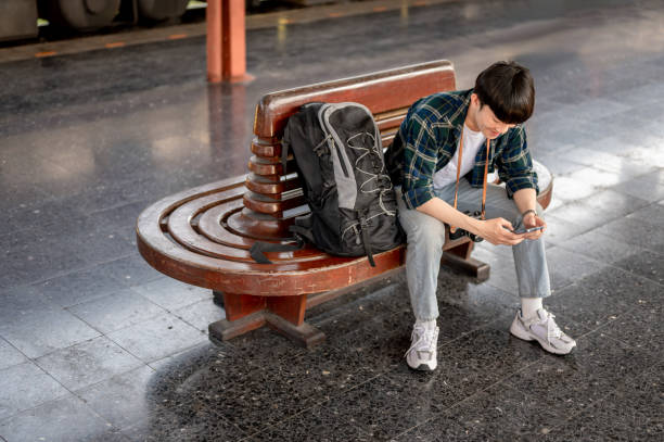 istock A young Asian male traveler is using his smartphone while waiting for his train at a railway station 1933762706