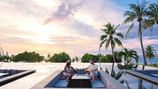 couple watching the sunset in an infinity pool on a luxury vacation in Thailand, man and woman watching the sunset on the edge of a pool in Thailand on vacation