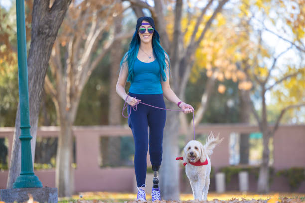 A happy woman with a prosthetic leg walking her dog at the park.