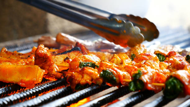 istock BBQ Barbecue grilled meat stick on fire flame with hot charcoal cooking outside. Beef grilling picnic outdoor with smoke bacon spicy sausage for party. Grill pork bbq on fire flame 1933799663