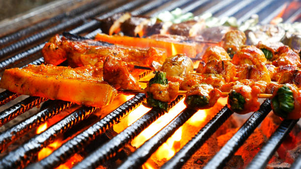 bbq barbecue gegrilltes fleisch auf feuerflamme mit heißer holzkohle kochen draußen. rindfleisch grillen picknick im freien mit rauch, speck, würziger wurst für die party. grillen sie schweinefleisch bbq auf feuerflamme - barbecue grill broiling barbecue vegetable stock-fotos und bilder