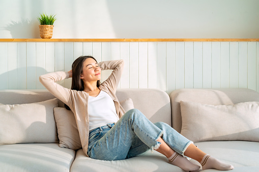 Carefree Asian woman relaxing and sitting on a sofa at home in the morning