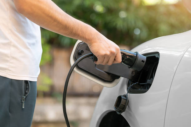 istock Hand inserts the electrical connector to charge the batteries with a blurred background of outdoor natural greenery. eco and clean energy concept. alternative clean and sustainable energy. save world 1933807587