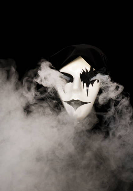 istock Cloak covered hand made mask with smoke pouring from eyes and background 1933898571