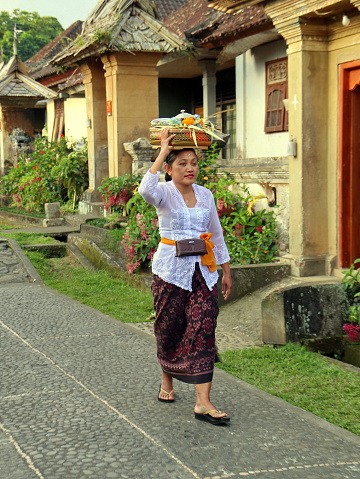 Bali, Indonesia - June 28, 2023 : Balinese woman walks up the village carrying basket on her head