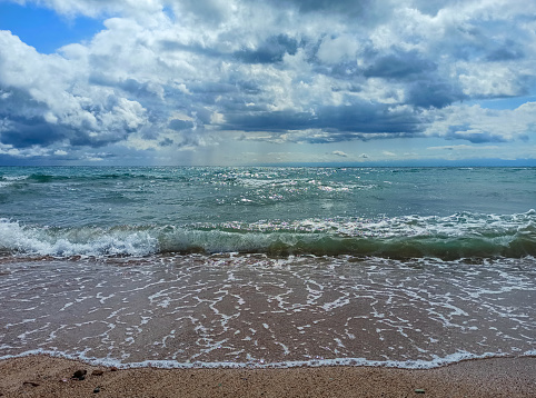 Cumulus clouds over the sea. Dramatic seascape. Waves on the shore. Kyrgyzstan, Lake Issyk-Kul.