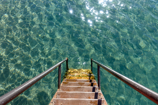 The wooden steps of the pier descend into clear blue water. Pier in the sea.