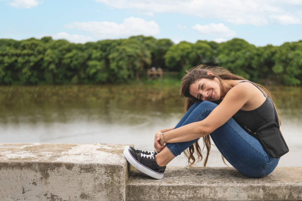 beautiful young woman smiling, casually dressed, sitting by a mountain lake