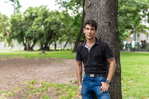 Man posing in a park leaning on a tree