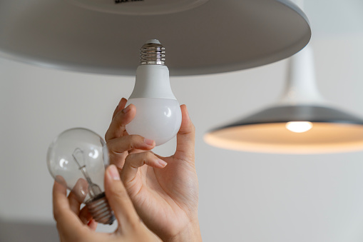 A young woman is changing a light bulb from an incandescent bulb to an LED bulb.