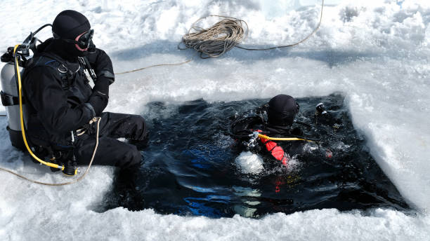 Two men equipped for winter under ice diving are swimming in an ice hole, tightened with a safety rope, ready to immerse, bubbles coming up from water