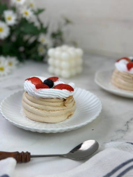 istock Two mini pavlova cakes from meringue and mascarpone decorated with fresh peach, figs, blackberries and blueberries on a white background. Close up. Confectionery, recipe, menu. Meringue summer dessert 1934078925