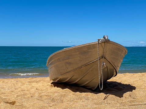 Small metal boat on a golden sand beach with blue water and waves under a blue sky.
