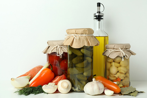 Jars of pickled vegetables and ingredients on white table