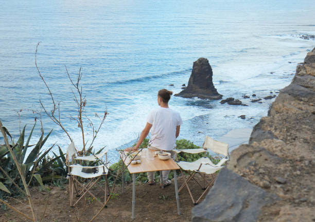 istock Dusk Serenity: Unrecognizable Young man at Cliffs Edge, Thinking and admiring Tranquil Ocean Waves Amidst Rocky Shoreline 1934140289