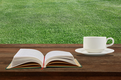 Coffee cup with book on the  wooden table against meadow.
Relaxing concept