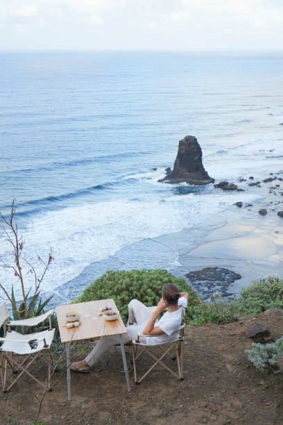 istock Solitary Reflection: Young man in White, Overlooking a beautiful Serene Ocean Landscape, Captured from Behind 1934156223