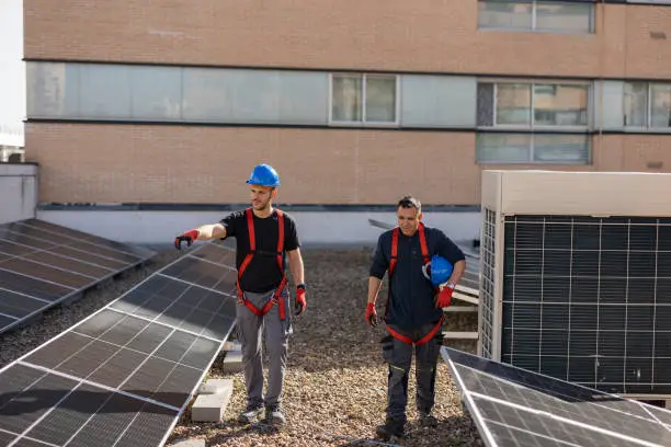 On house rooftops, a team of skilled workers labors with purpose, fitting solar panels like pieces of a renewable puzzle, bringing the power of the sun to households.