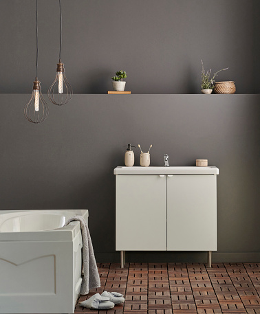 Modern bath room cabinet, sink, mirror and tub style grey wall background, vase of plant, laundry, towel and wooden stairs decorations.