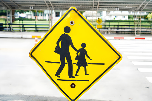 Picture of a traffic sign warning moving cars to be careful of people crossing the road at a school zebra crossing.