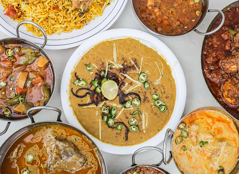 Chicken haleem, chicken karahi, biryani, beef nihari, curry pakora, chanay, aloo shimla mirch and keema isolated on grey background top view of pakistani and assorted indian spices food variety
