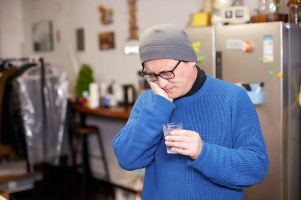 Portrait of man with toothache drinking ice water at home in winter