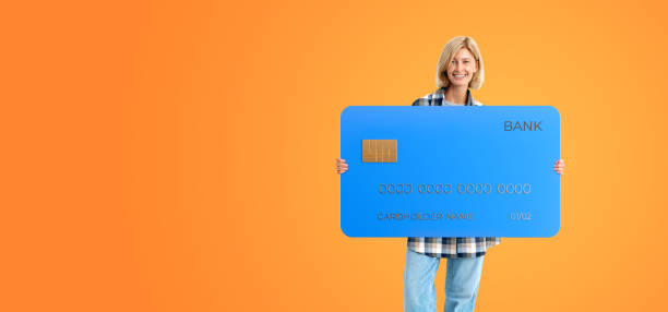 istock Smiling woman standing with credit card on empty orange background 1934239169