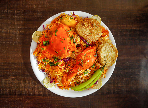 Spicy chicken biryani with shami kabab, potato, and lemon slice served in plate isolated wooden background top view indian spices and pakistani food
