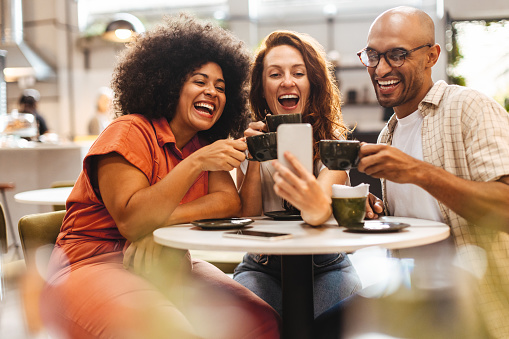 Trio of friends capture the moment with a fun selfie while enjoying each other's company over steaming cups of coffee in a comfortable cafe setting, surrounded by the aroma of freshly brewed coffee.