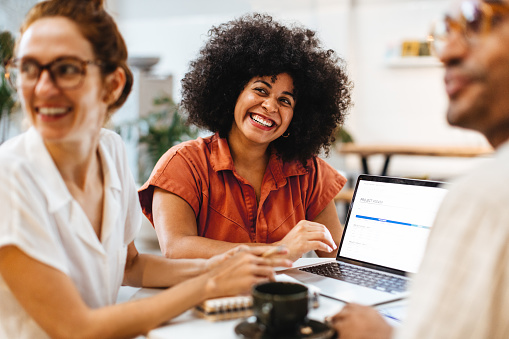 Group of happy remote professionals sitting in a cafe, engaged in a project and collaborating on ideas. Diverse business colleagues having a team meeting in a coffee shop.