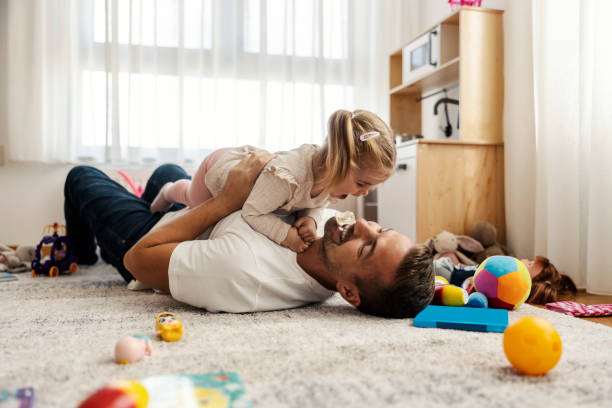 Dad is playing with his daughter on the floor at home and having fun time.