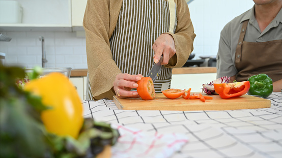 Senior woman housewife cutting fresh tomato on board while preparing healthy lunch in kitchen.