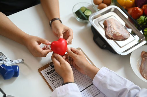 Above view of nutritionist holding red heart shape during conversation with patient at clinic. Heath care concept.
