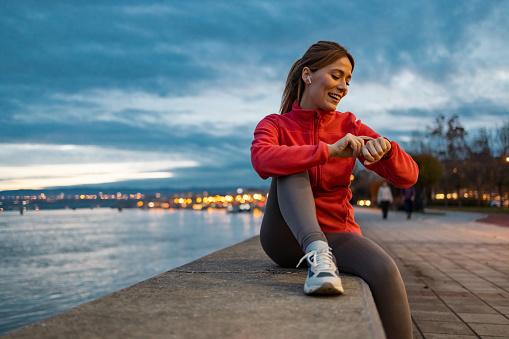 Happy athletic woman in sportswear looking at her smartwatch outdoors.