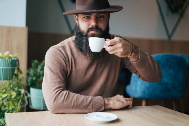 A happy young man with a hat is enjoying a coffee break