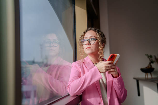 istock Woman using mobile phone next to window at her office 1934304563