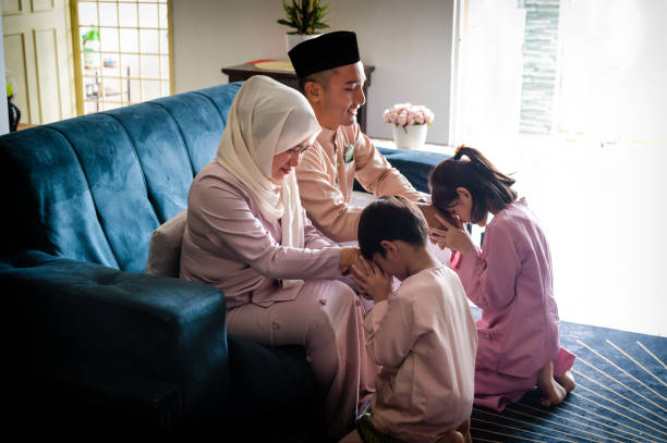 Young Malay Muslim boy and girl in traditional costume showing apologize gesture to their parents during the Hari Raya Aidilfitri Celebration. Young Muslim family embraces during Hari Raya Aidilfitri Celebrations. malay couple full body stock pictures, royalty-free photos & images