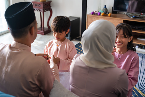 Young Muslim boy and girl receiving green packets from their parents on the 1st day of Hari Raya Aidilfitri Celebration.
