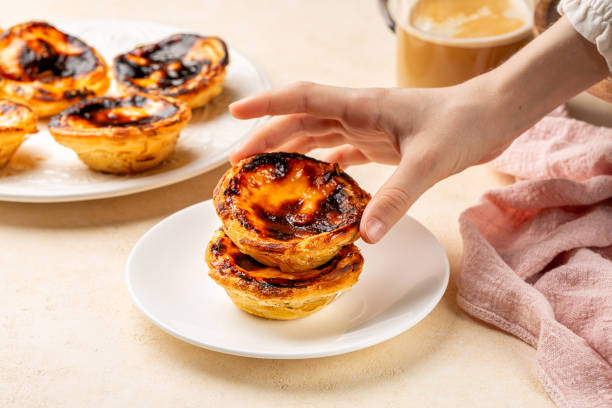 comer pastel de nata o pastel de belem, tarta portuguesa de natillas de huevo al horno. muchachas de la mano sosteniendo pasteles. desayuno dulce con taza de café en el fondo. - egg tart fotografías e imágenes de stock