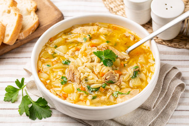 Homemade chicken orzo soup in a white plate, fresh bread.