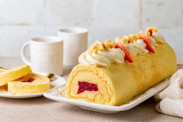 Photo of Rolled sponge cake filled with custard cream and berry jelly, decorated with whipped cream cheese and strawberries. Swiss or jelly roll cake, roulade or Swiss log. White background.