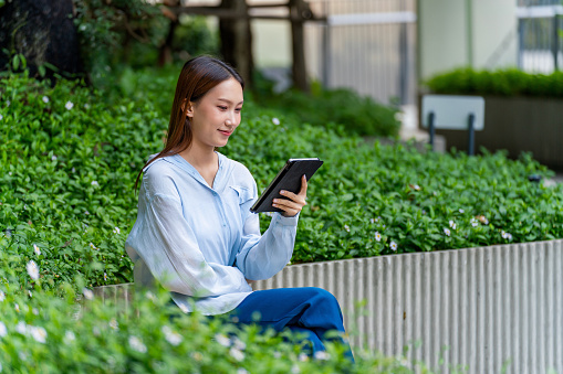 Remote Work Oasis: Asian Woman Embraces Flexibility, Working with Tablet in the Tranquil Setting of an Outdoor Park